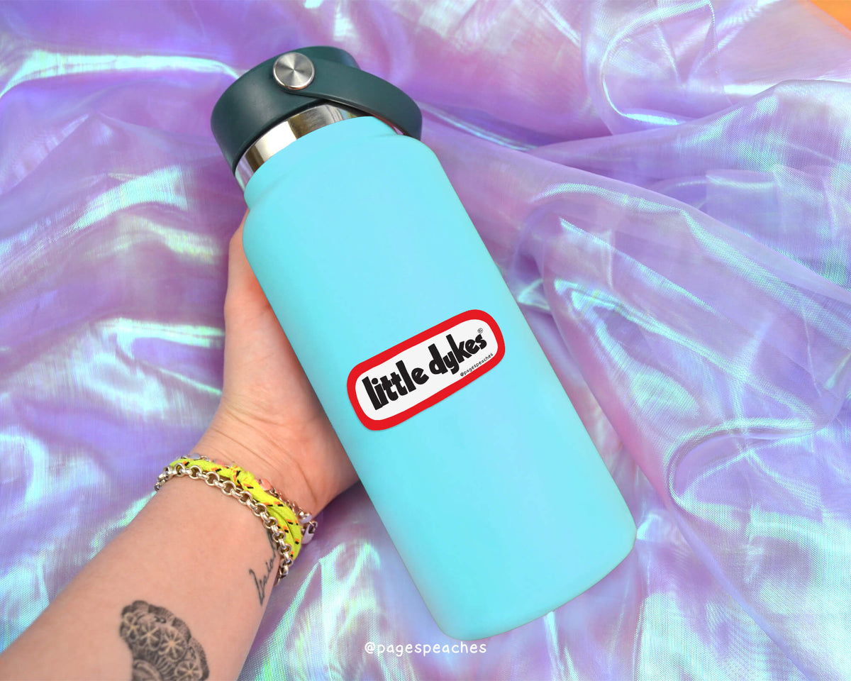 A person&#39;s hand holding a blue water bottle with a red and white sticker on it, against a purple fabric background.