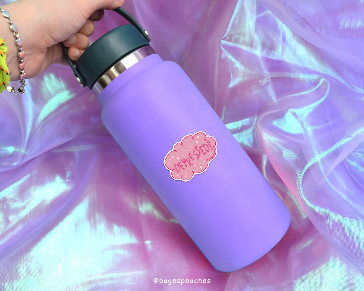 A purple water bottle with a pink cloud-shaped sticker on it, held in a hand against a purple fabric background.