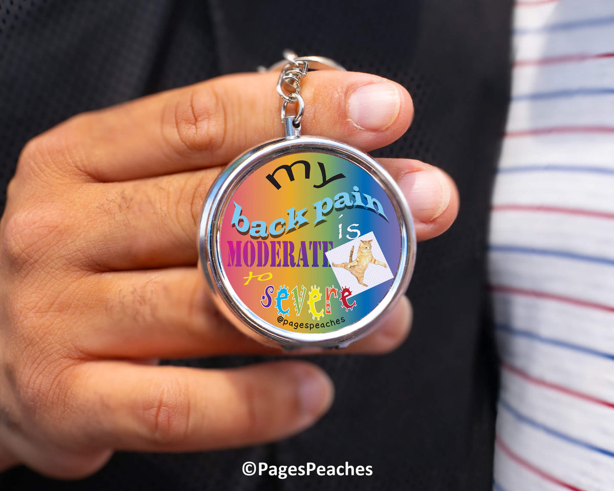 A person is holding a colorful keychain with the text &quot;MY back pain is moderate to severe&quot; printed on it.