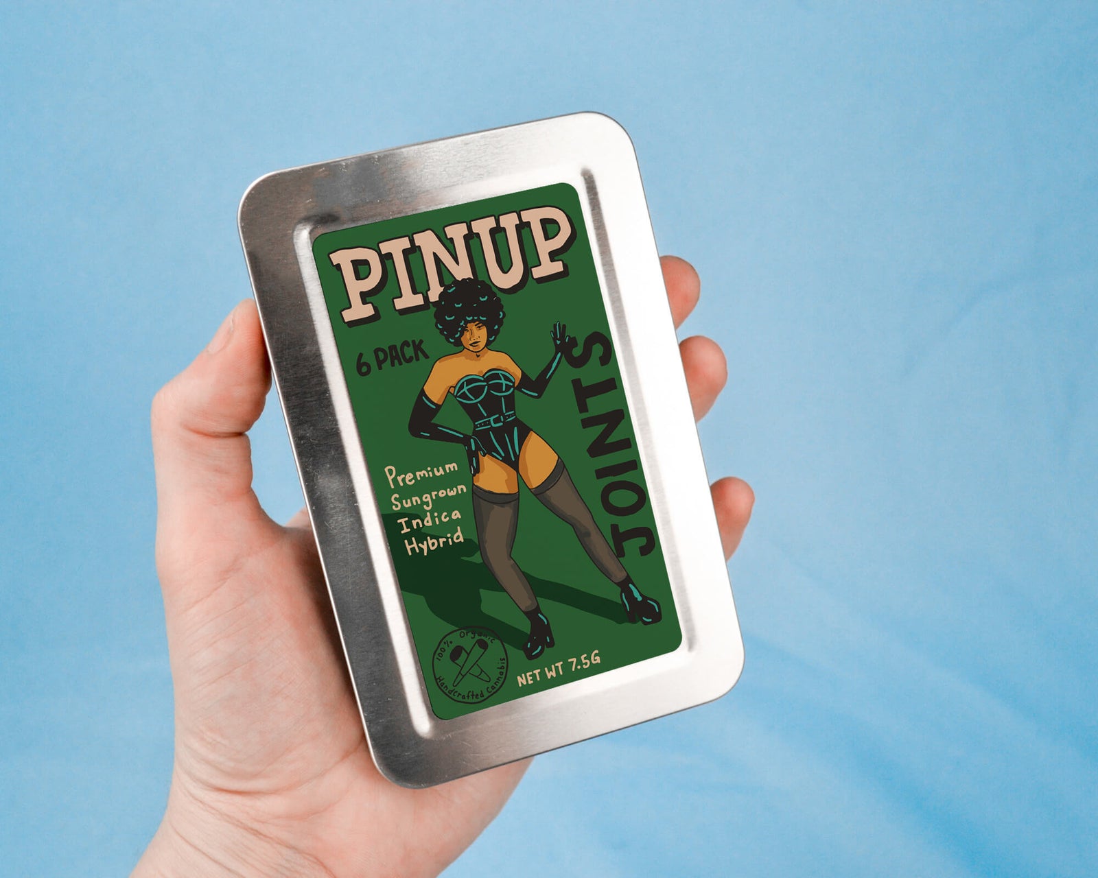 a hand holding a tin up to a picture of a pinup