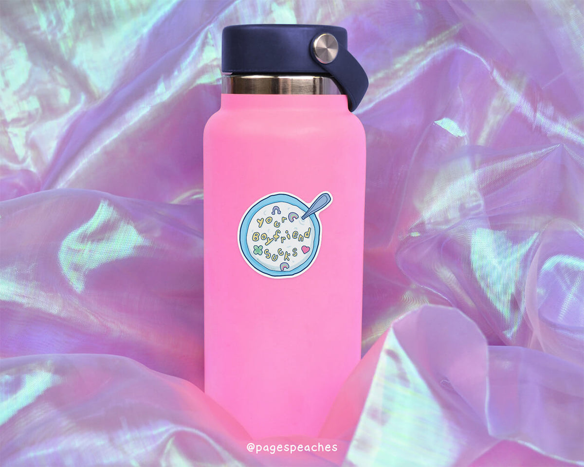 A pink water bottle with a cartoon cereal bowl sticker on it, placed on a purple fabric background.