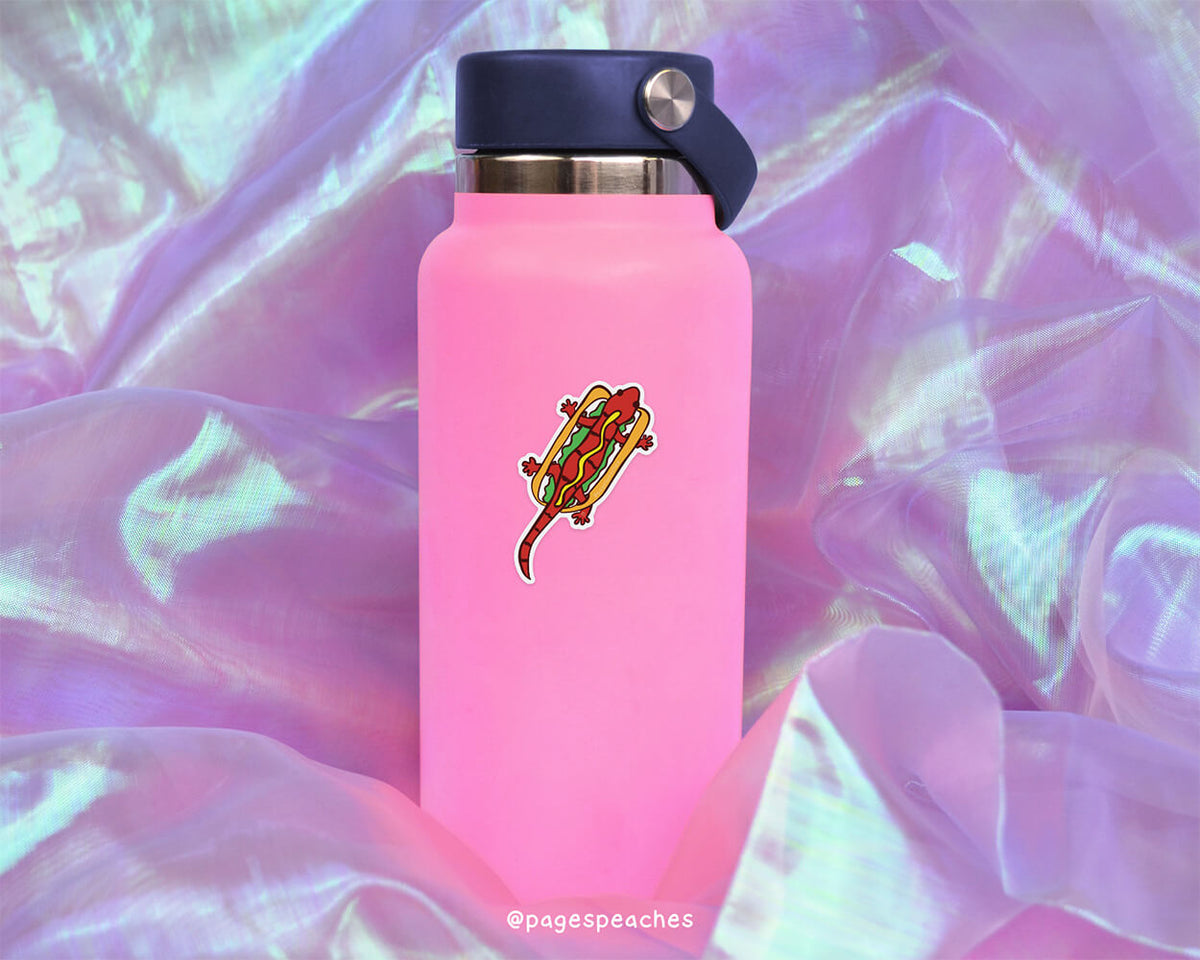 A pink water bottle with a sticker of a cartoon lizard on it, placed on a purple fabric background.