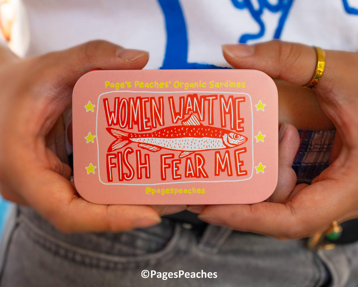A person is holding a pink tin can with a fish and the text &quot;Women Want Me Fish Fear Me&quot; printed on it.