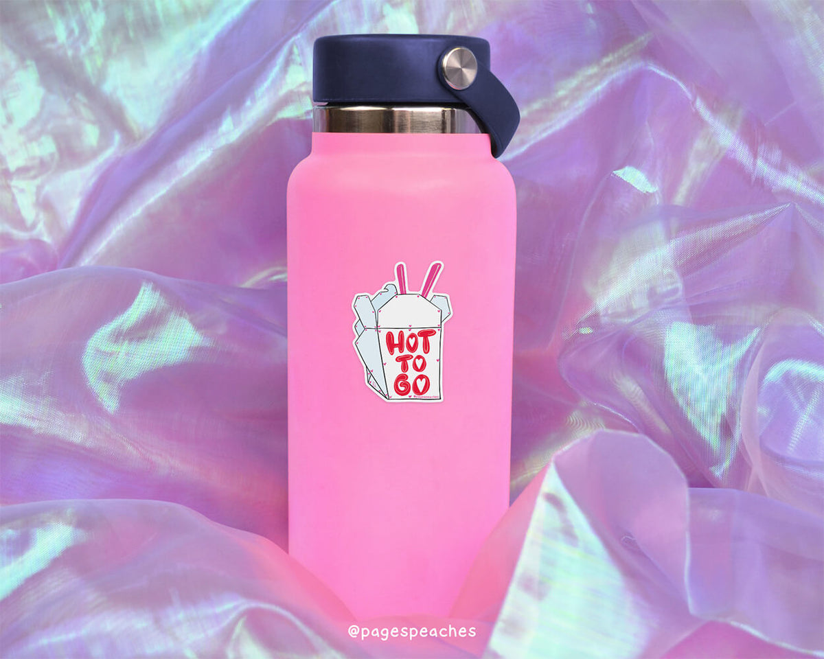 A pink water bottle with a sticker that says &quot;HOT TO GO&quot; is placed on a purple fabric background.