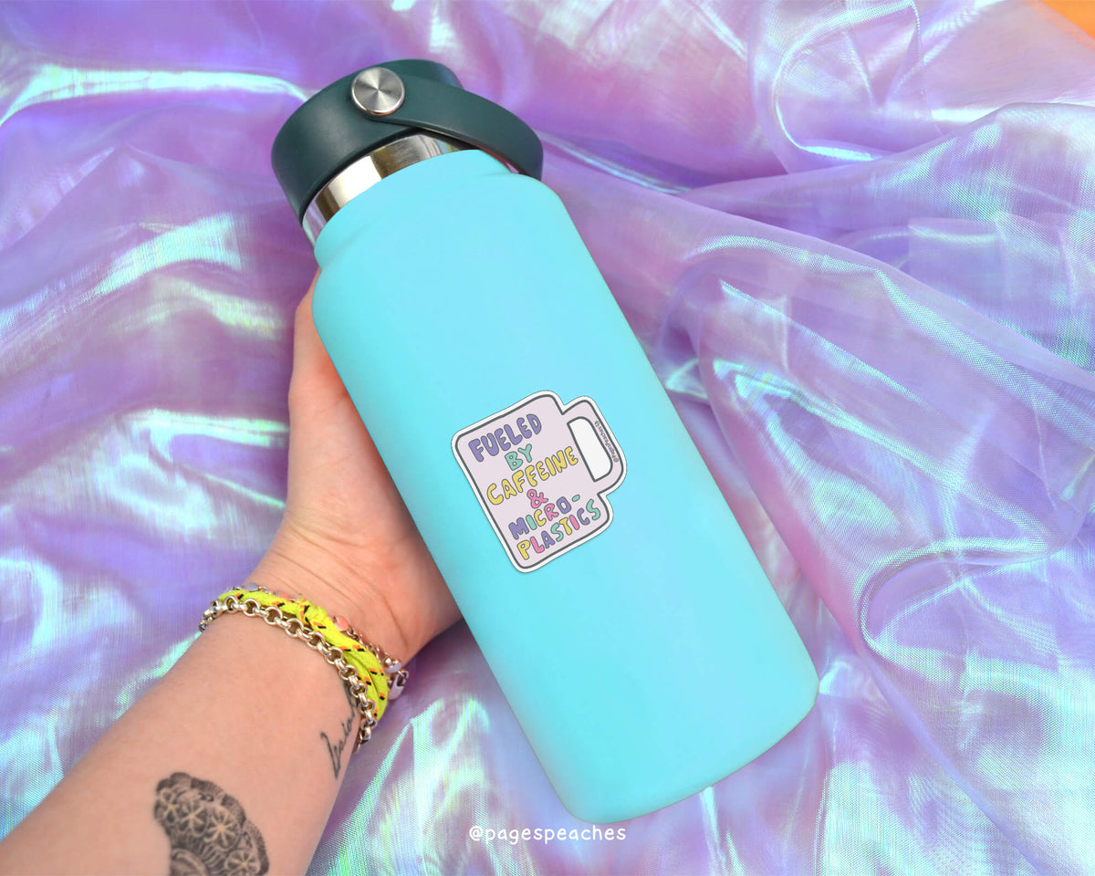 A person&#39;s hand holding a blue water bottle with a sticker on it, against a purple fabric background.