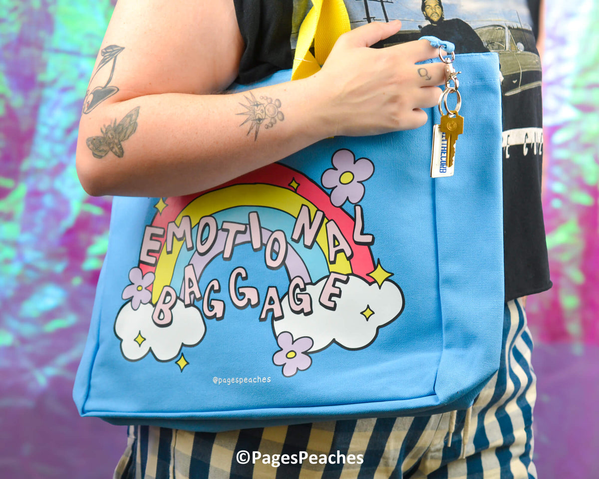Blue bag with &#39;Emotional Baggage&#39; design held by a person against a colorful background