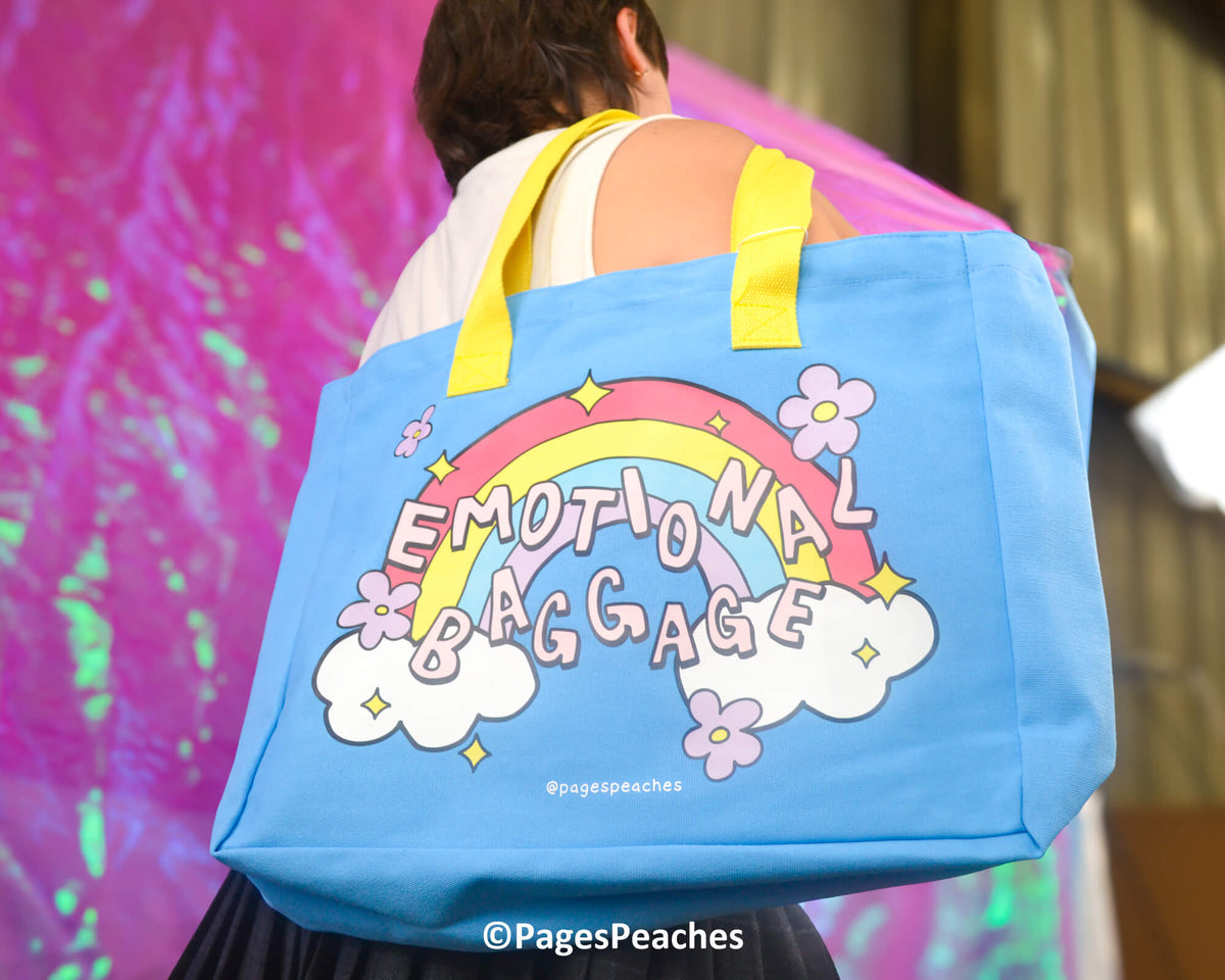 Person carrying a blue tote bag with a rainbow and cloud design, featuring the text &#39;Emotional Baggage&#39;.