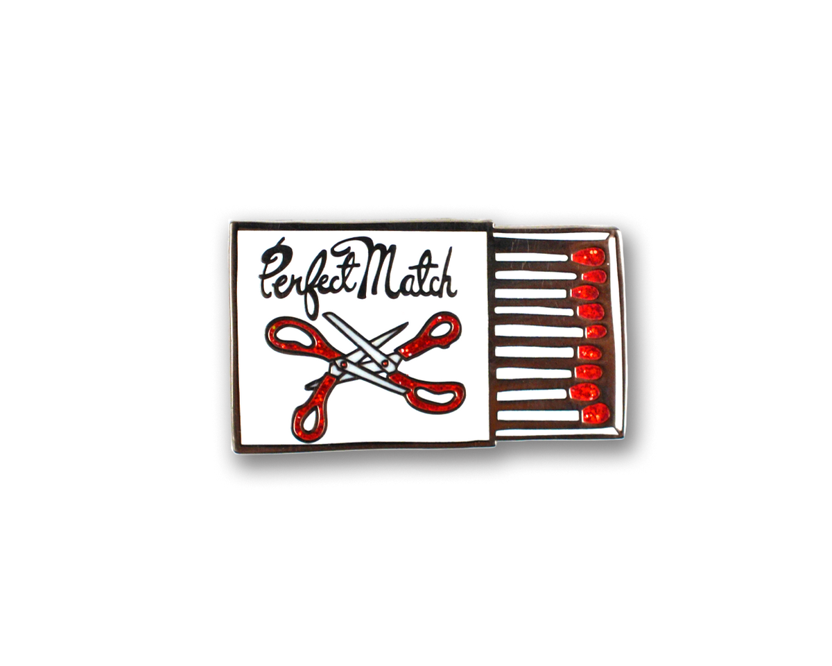 Matchbox-shaped enamel pin with scissors and 'Perfect Match' text on a white background