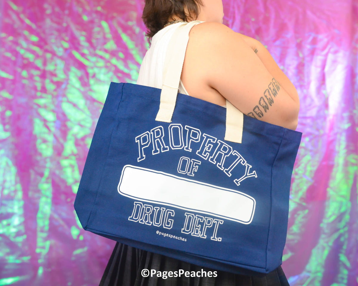 Person holding a blue tote bag with &#39;Property of Drug Dept.&#39; text against a colorful, abstract background.