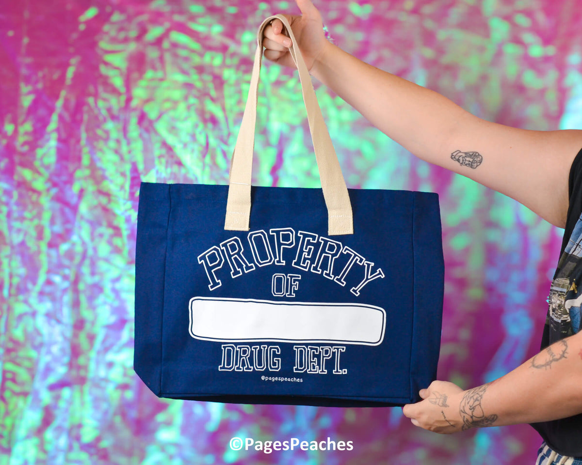 Person holding a blue tote bag with &#39;Property of Drug Dept&#39; text against a colorful, abstract background.