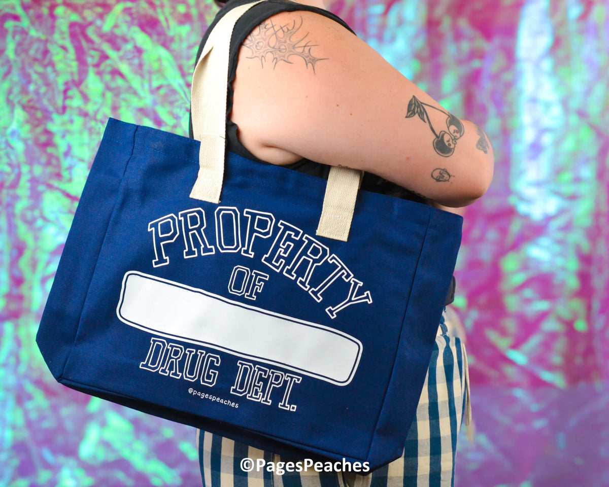 Person holding a blue tote bag with &#39;Property of Drug Dept&#39; text against a colorful background