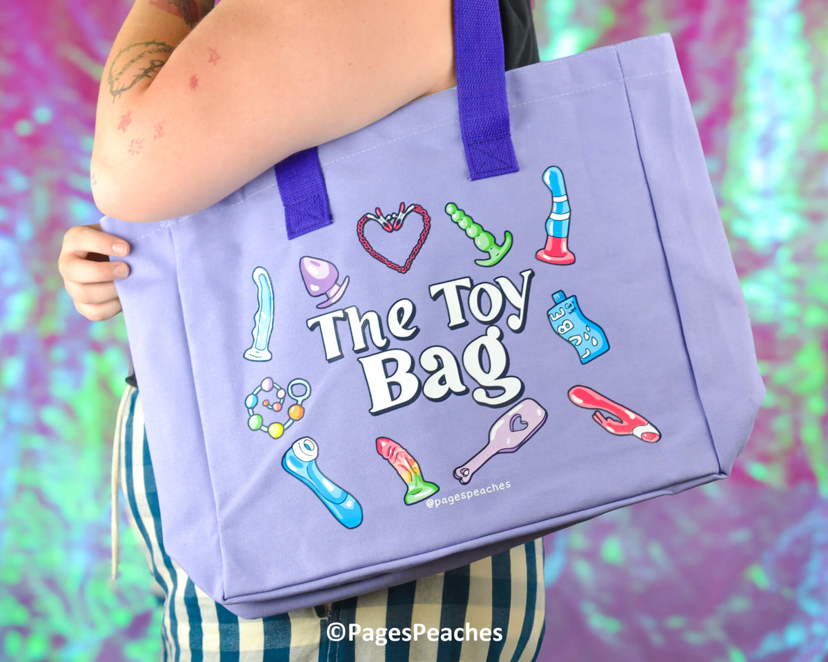 Purple tote bag with colorful illustrations and &#39;The Toy Bag&#39; text, held by a person against a multicolored background.