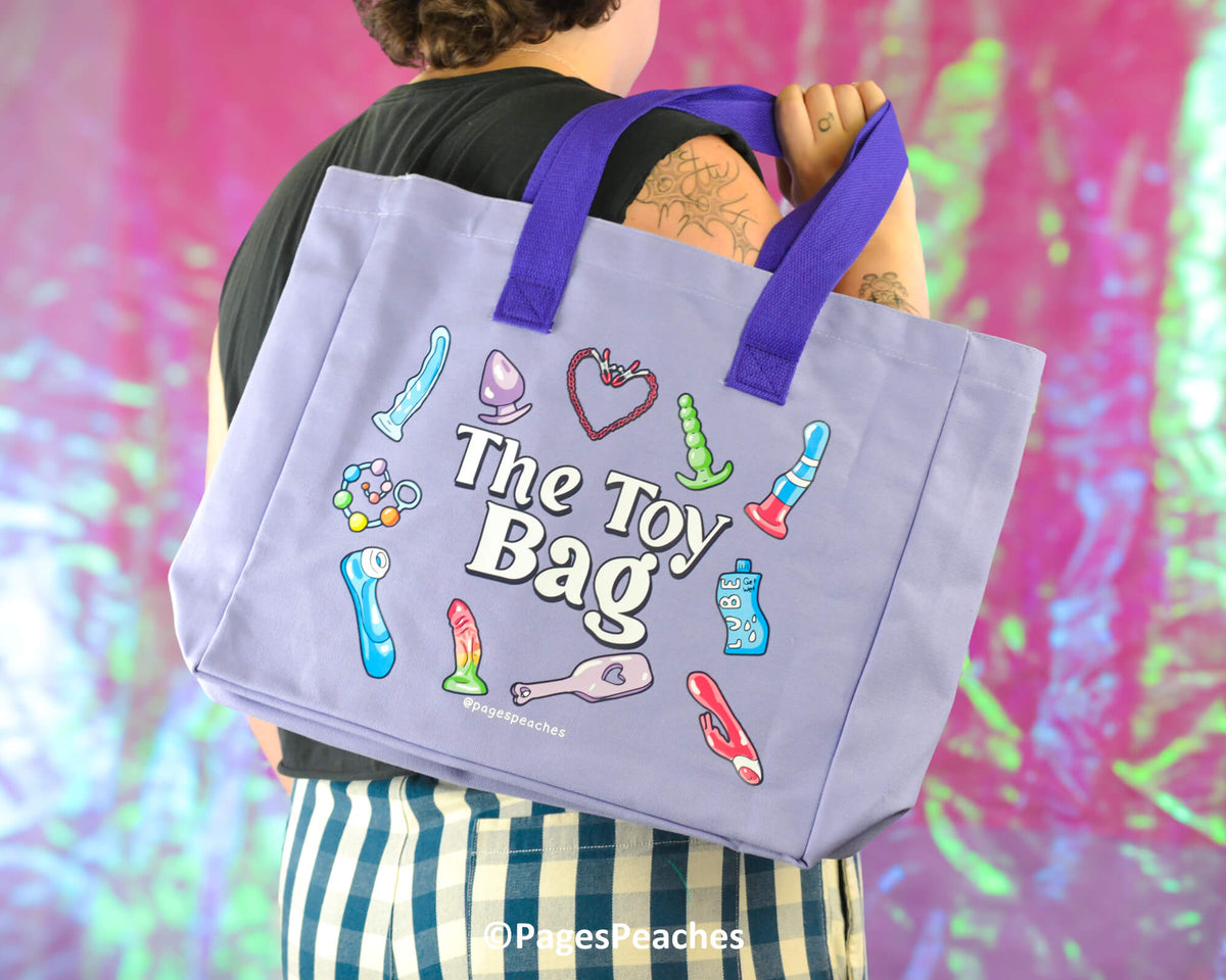 Person holding a tote bag labeled &#39;The Toy Bag&#39; with colorful illustrations against a multicolored background.