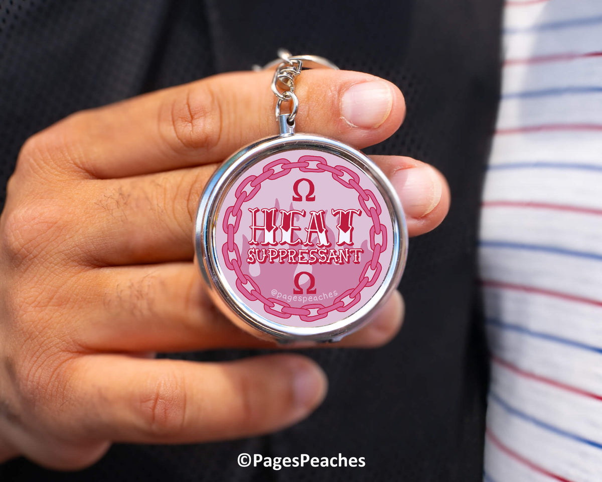 A person is holding a keychain with a circular design featuring the text &quot;HEAT SUPPRESSANT&quot; and an Omega symbol.