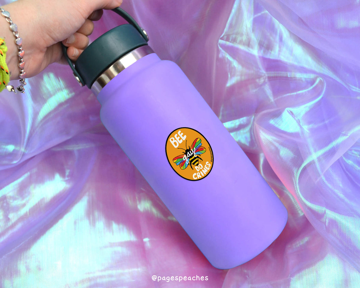 A purple water bottle with a sticker on it, placed on a pink fabric background.