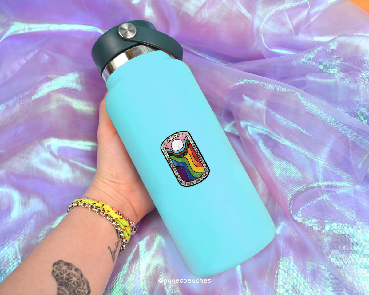 A person&#39;s hand holding a blue water bottle with a colorful sticker on it, against a purple fabric background.