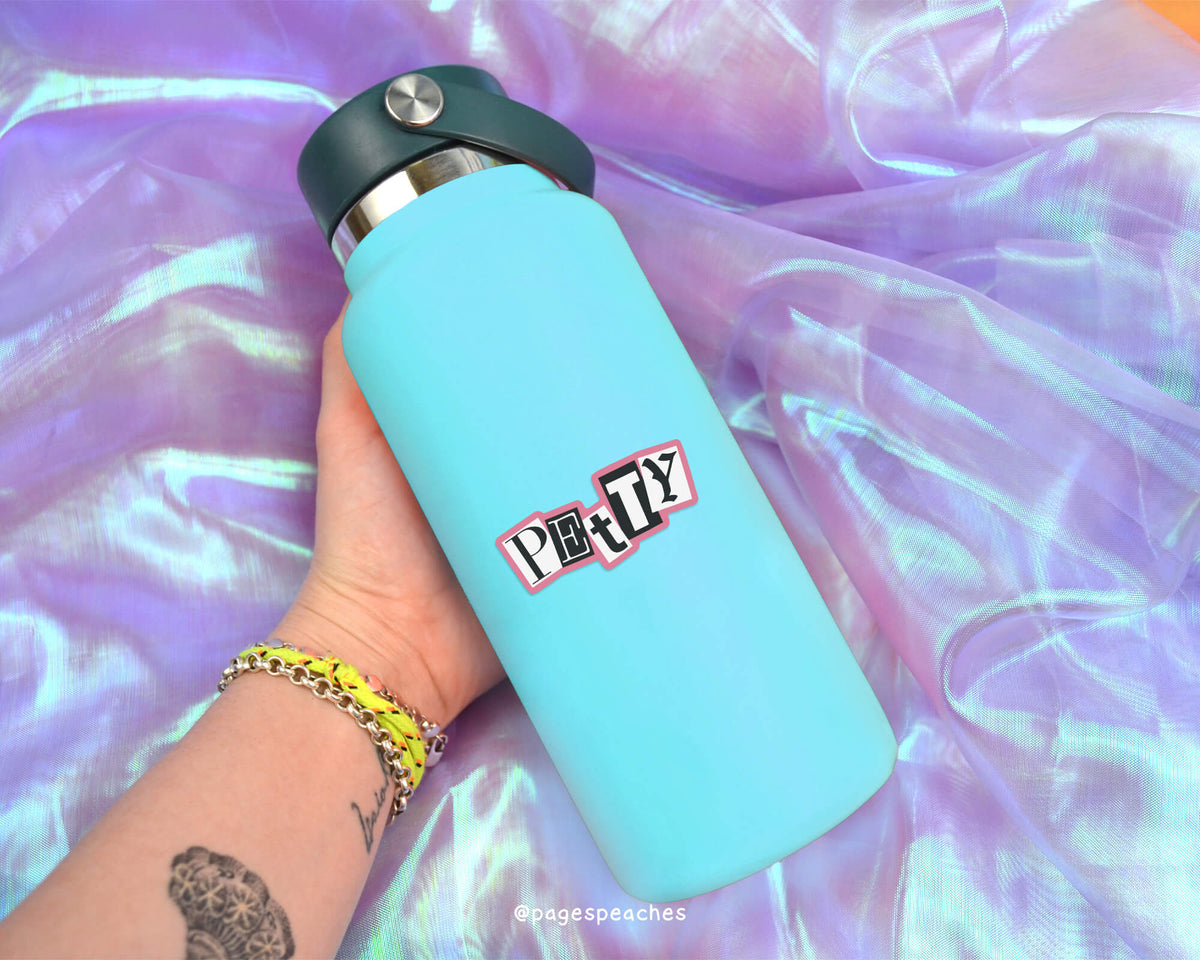 A person&#39;s hand holding a blue water bottle with a sticker on it, against a purple fabric background.