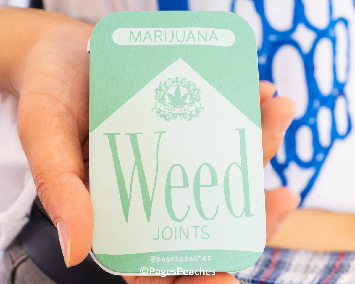 A person is holding a mint-colored box with the word &quot;Marijuana&quot; written on it, and the word &quot;Weed&quot; below it.