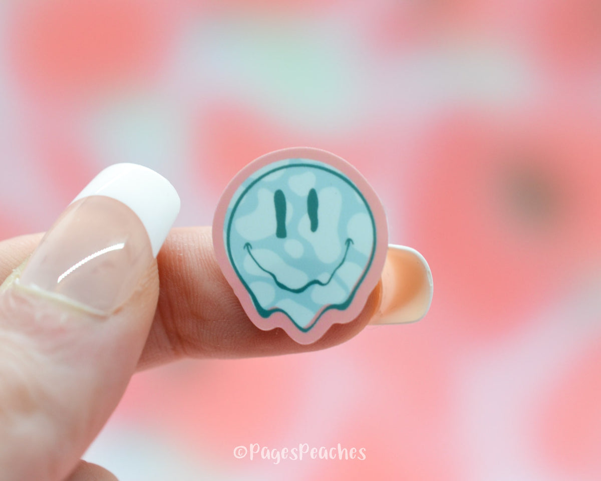 Small Sticker of a Cow Print Smiley Face stuck to a finger