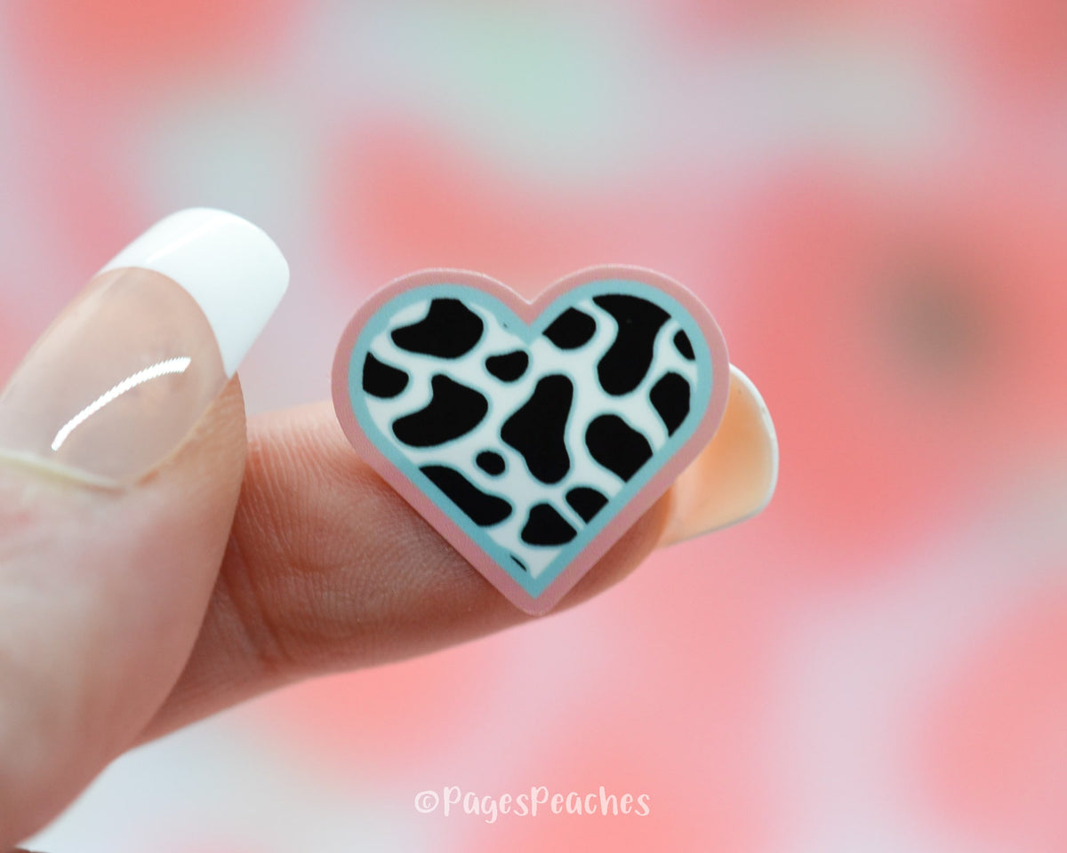 Small Sticker of a pink and blue cow print heart stuck on a finger
