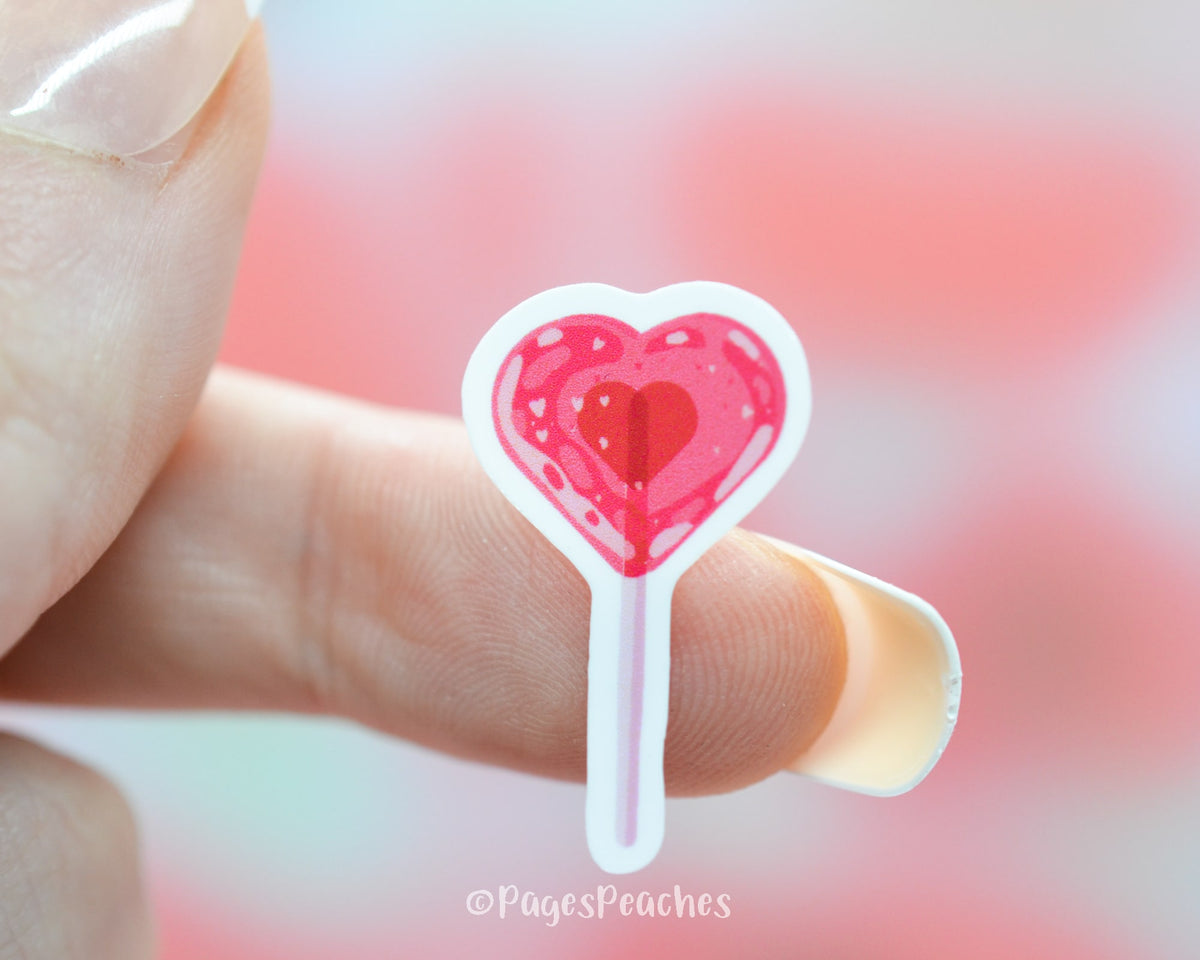 Small Sticker of a heart shaped lollipop stuck to a finger