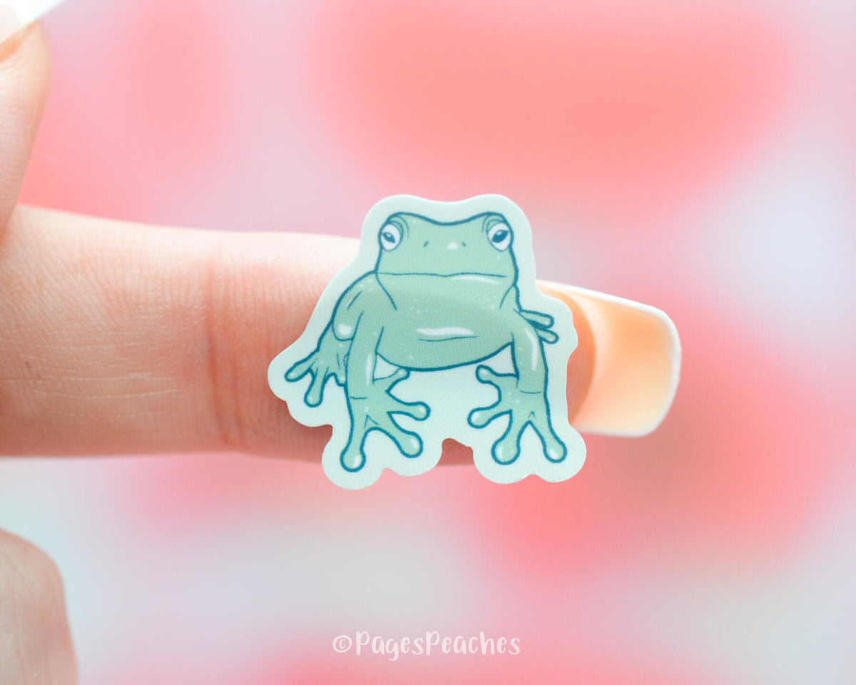 Small Sticker of a green frog stuck to a finger