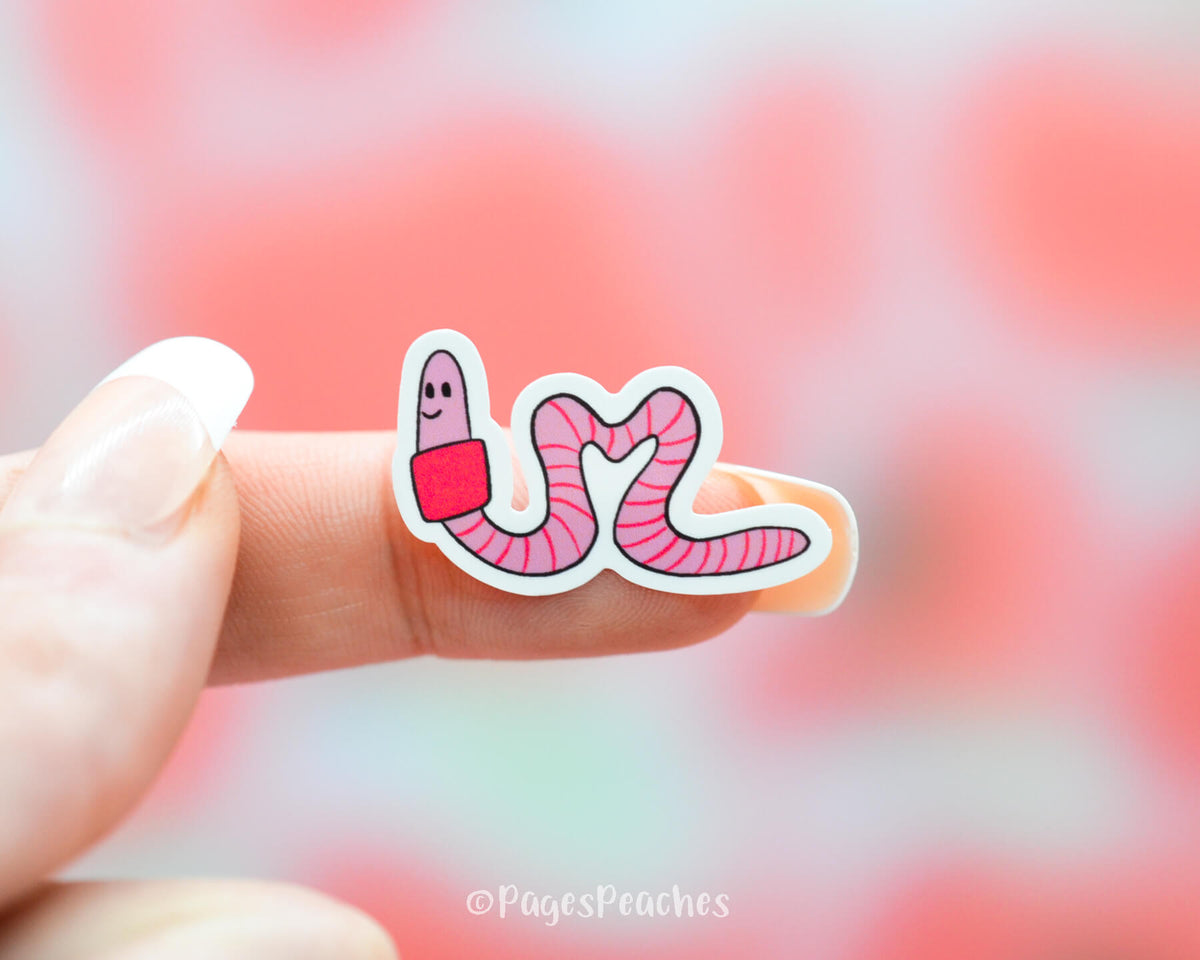 Small Sticker of a Pink Heart Worm that is stuck to a finger