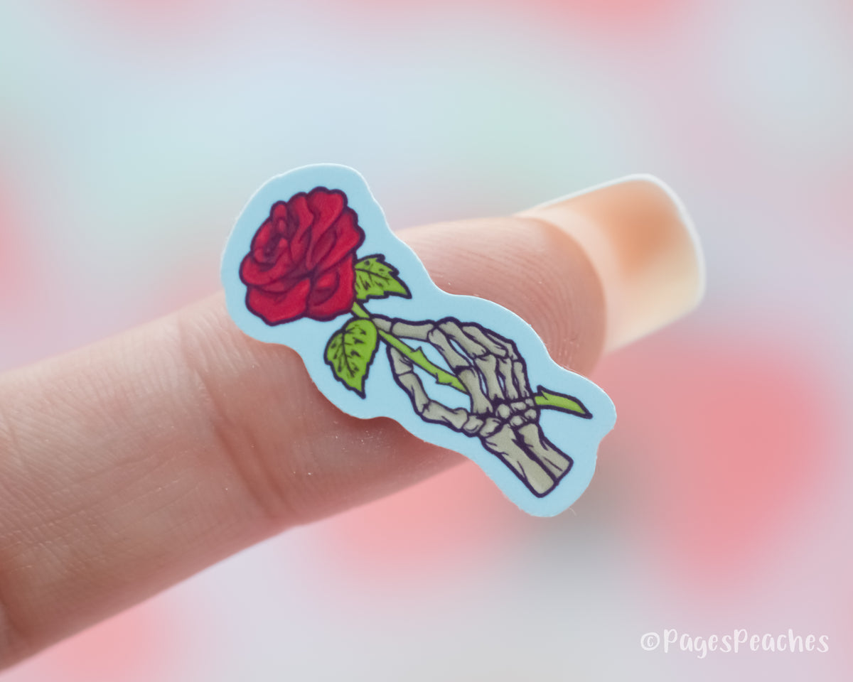 Small Sticker of a skeleton hand holding a rose stuck to a finger