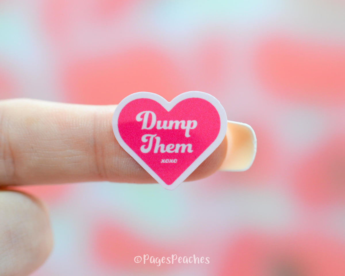 Small Pink Heart Sticker that says Dump Them stuck to a finger