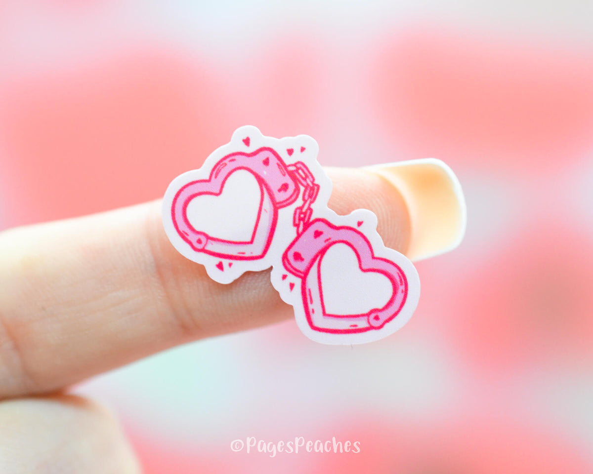 Small Sticker of Pink Heart Shaped Handcuffs stuck to a finger