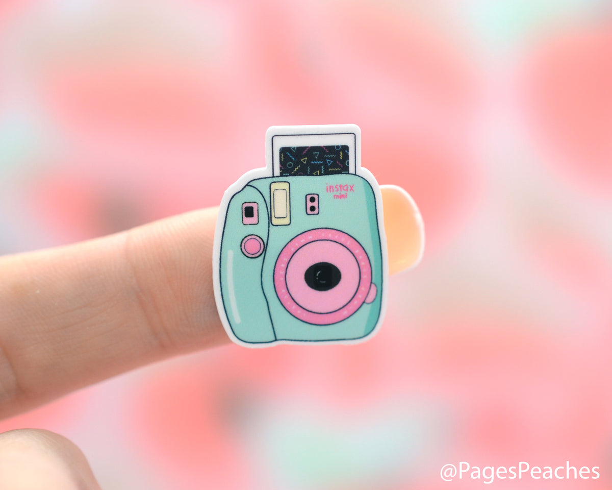 Small Sticker of a blue and pink instant camera stuck to a finger